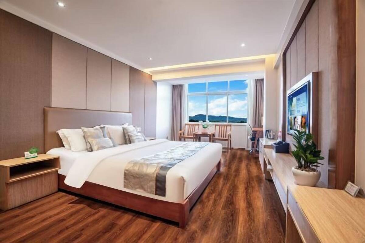 A modern hotel room with a large bed, a desk, and a view of the mountains.