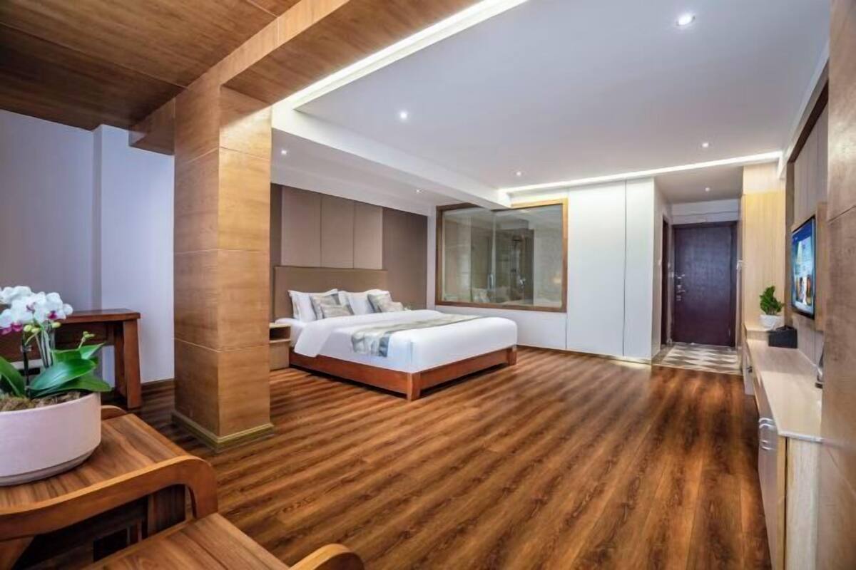 A modern bedroom with a large bed, wooden flooring, and a large window.
