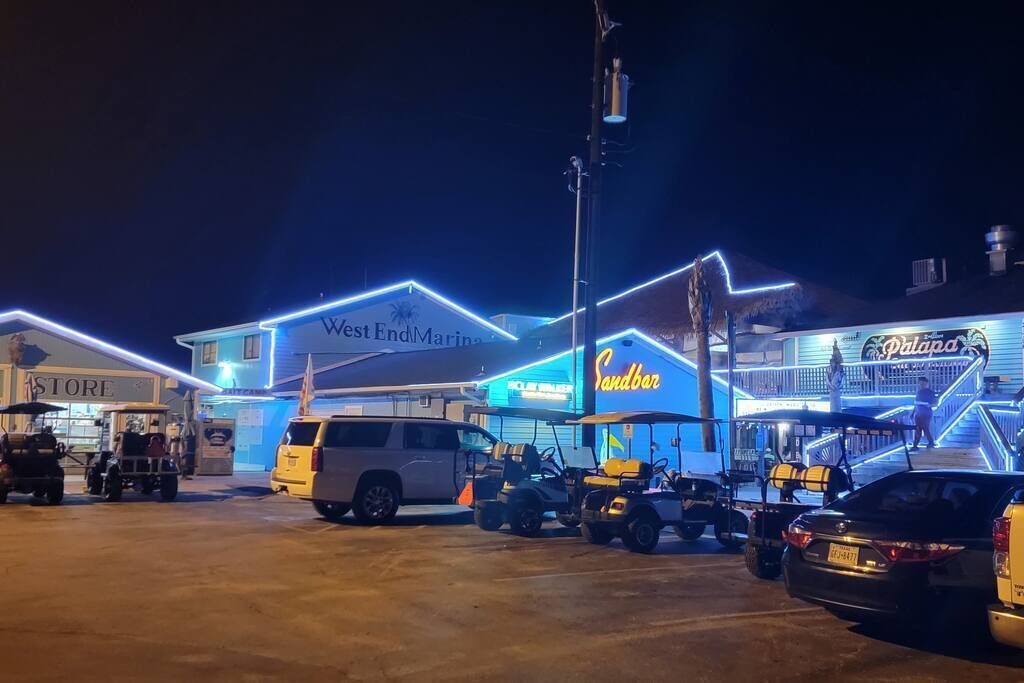 A brightly lit commercial area with a store named "West End Marine" and a bar called "Sandbar."