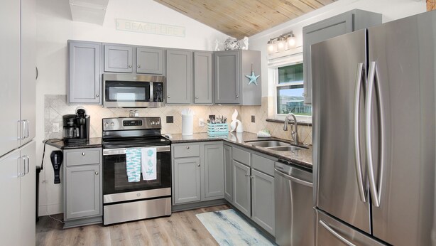 A modern kitchen with grey cabinets, stainless steel appliances, and a wooden ceiling. - 6 Bedroom + Crows Nest - Beach View (Galveston)