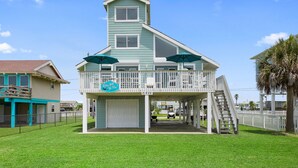 A two-story building with a balcony, a garage, and a sign that reads "Rolling With The Flow." - 6 Bedroom + Crows Nest - Beach View (Galveston)