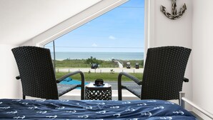 A balcony with wicker chairs, a small table, and a view of the beach and ocean. - 6 Bedroom + Crows Nest - Beach View (Galveston)