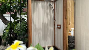 A wooden shower enclosure with a bamboo backdrop, a stone sculpture, and a small shelf with bottles.