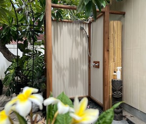A wooden shower enclosure with a bamboo backdrop, a stone sculpture, and a small shelf with bottles. - Lovely Private Kailua Cottage (Kailua)