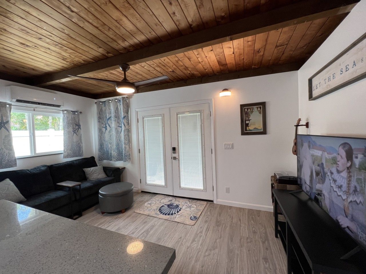A living room with a wooden ceiling, a black sofa, a coffee table, a TV, and a door with glass panels.