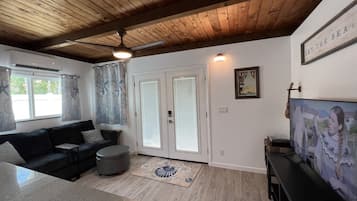 A living room with a wooden ceiling, a black sofa, a coffee table, a TV, and a door with glass panels.