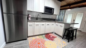 A modern kitchen with stainless steel appliances, white cabinetry, and a colorful rug.