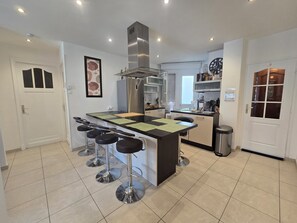 Una cocina moderna con una isla central, taburetes de bar, electrodomésticos de acero inoxidable y un reloj en la pared.