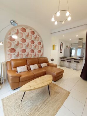 A modern living room with a brown leather sofa, a wooden coffee table, and a kitchen area in the background.