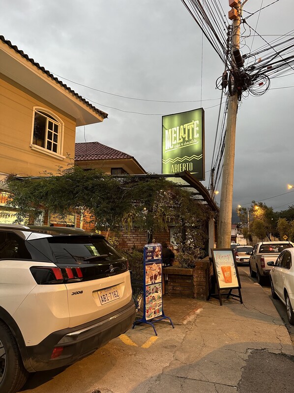 A street view with parked cars, a building with a sign for 'Melatte café & chocolate', and a billboard advertising 'Paradise'. - Cozy and beautiful mini suite (Cuenca)