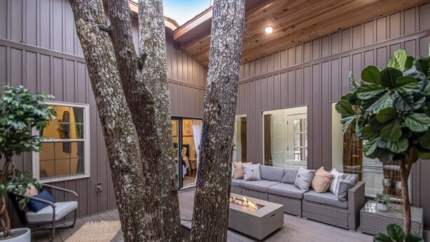 A modern outdoor living area with a built-in fire pit, seating, and large windows. - Creek Treehouse Atrium Hot Tub Buffalo (St Joe)