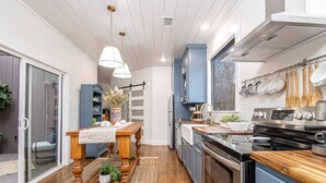 A modern kitchen with wooden flooring, a central island, and blue cabinets. - Creek Treehouse Atrium Hot Tub Buffalo (St Joe)