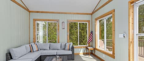 A sunlit room with a large sectional sofa, a small table, and a ceiling fan.