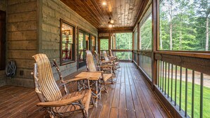 A wooden deck with outdoor seating and large windows overlooking a forest.