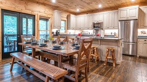 A wooden interior with a dining table set for four, wooden benches, and a kitchen area with stainless steel appliances.