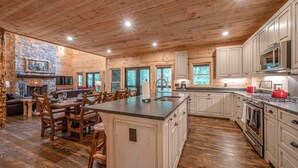 A spacious kitchen with wooden cabinetry, a central island, and a stone fireplace.