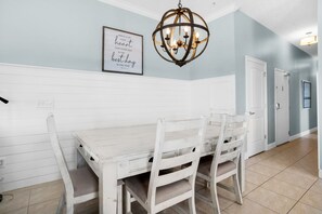 Un coin repas avec une table et des chaises en bois peintes en blanc, un lustre et une citation encadrée accrochée au mur.