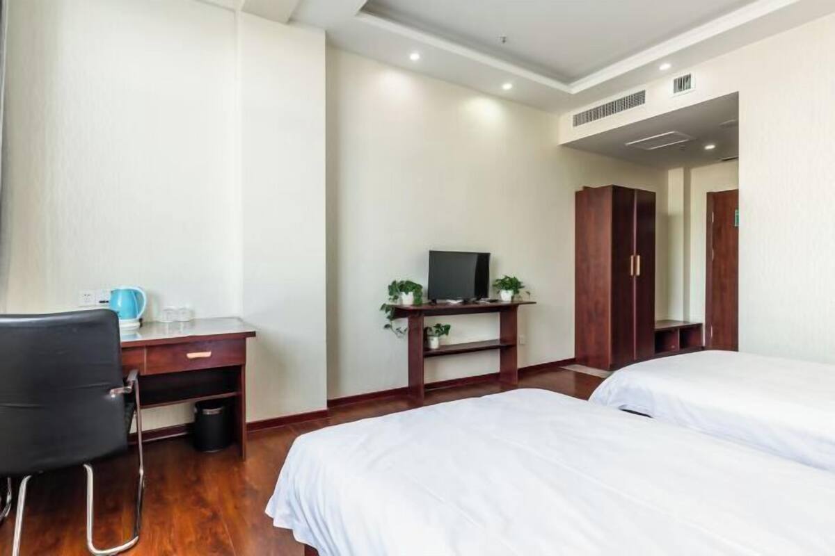 A hotel room with a desk, two beds, a TV, and a wardrobe.