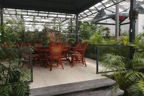 An outdoor patio with wicker furniture and a glass roof, surrounded by various plants. - Tianyuan Jibushi Hot Spring Hotel (Haicheng)