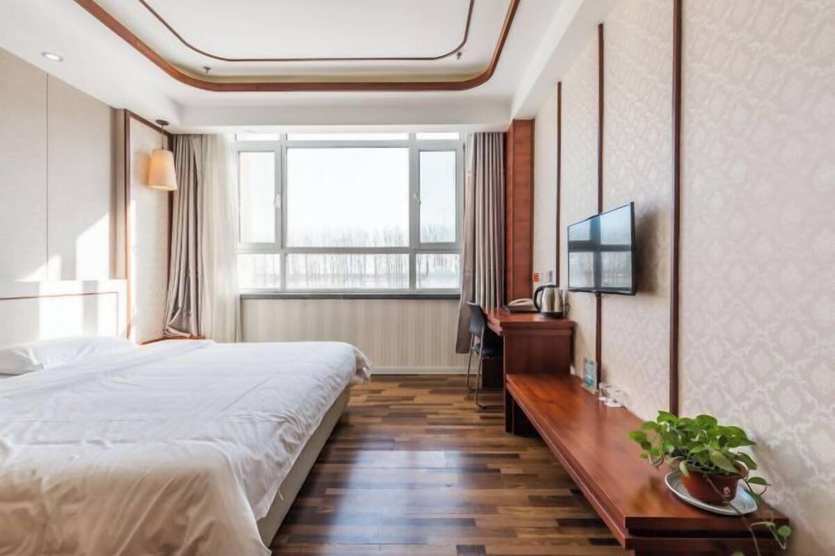 A hotel room with a large bed, a desk with a chair, a television, and a window with curtains.