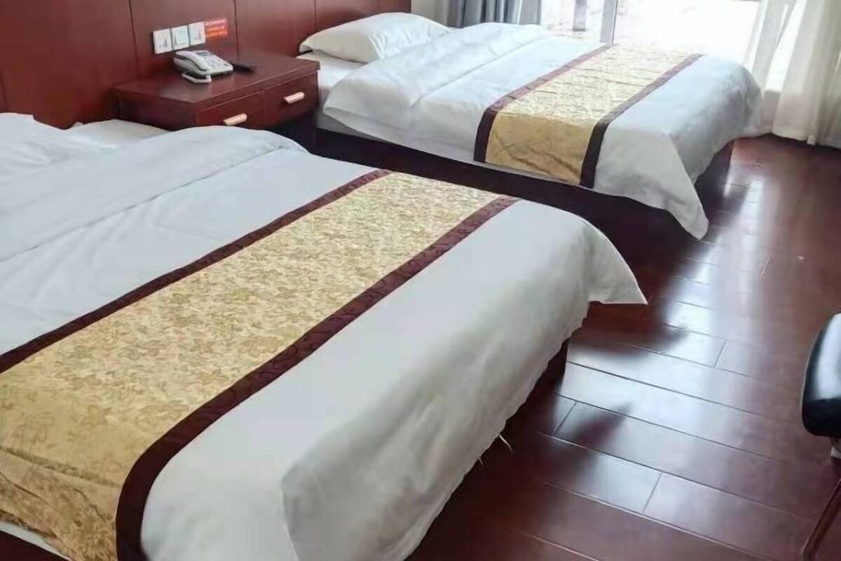 A hotel room with two beds, a wooden floor, a nightstand with a phone, and a window with curtains.