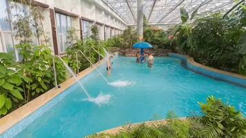 An indoor swimming pool with a glass ceiling, surrounded by lush greenery.