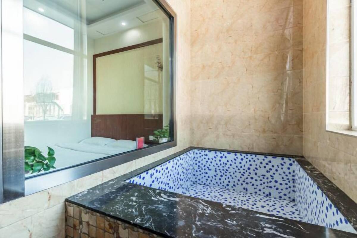 A bathroom with a large mirror, a bathtub with a polka dot pattern, and a window with a view of the outside.