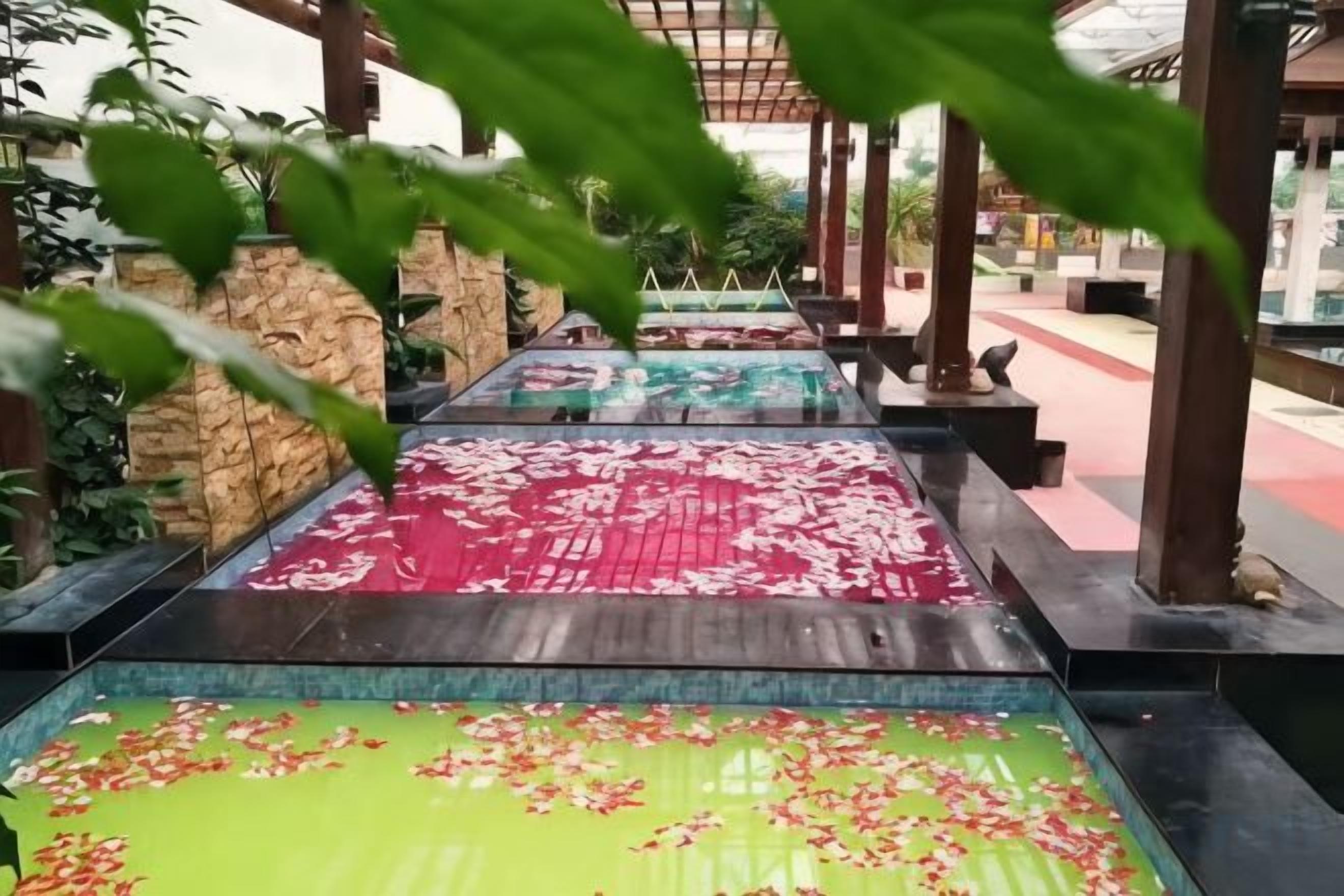 A series of rectangular water features with flower petals floating on the surface, surrounded by stone walls and wooden structures.