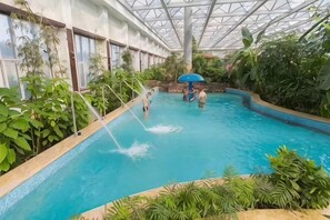 An indoor pool with a glass ceiling, surrounded by lush greenery. - Tianyuan Jibushi Hot Spring Hotel (Haicheng)