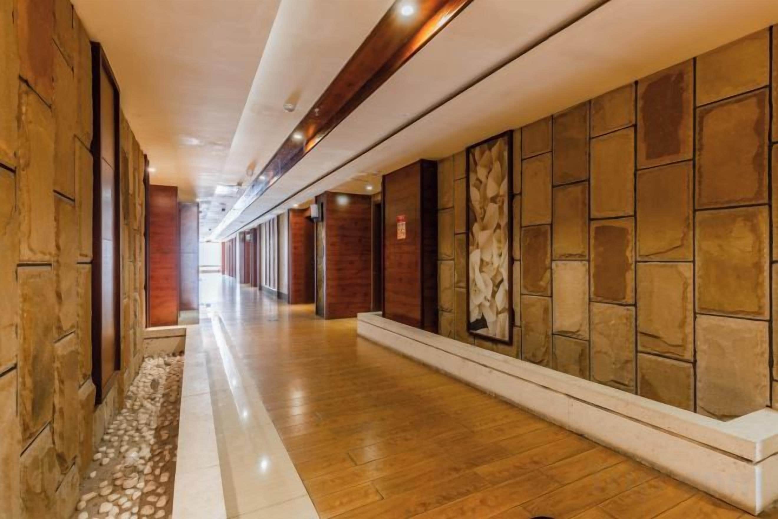A long, narrow hallway with a polished wooden floor, flanked by walls with a mix of textured and plain surfaces.