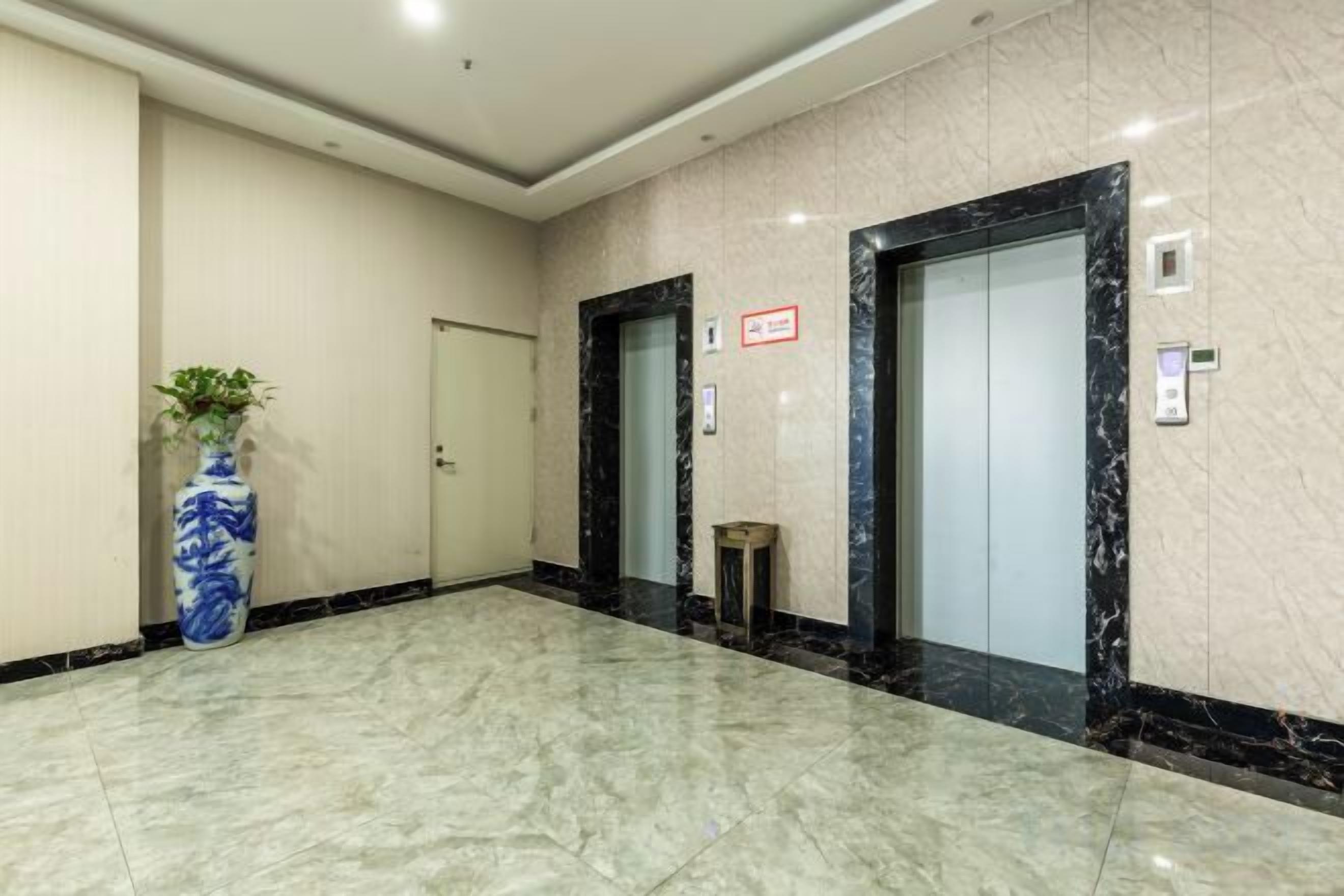 A lobby with a marble floor, a potted plant, and two elevators.
