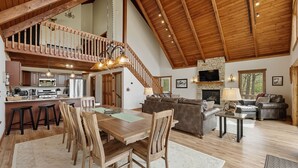 A spacious living area with a wooden ceiling, a dining table with chairs, a sofa, and a fireplace. - Fireplace Deck, Game Room & Mountain Vibes (McHenry)