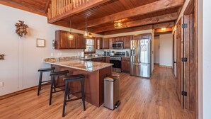 A spacious kitchen with wooden beams, stainless steel appliances, and a central island with bar stools. - Fireplace Deck, Game Room & Mountain Vibes (McHenry)