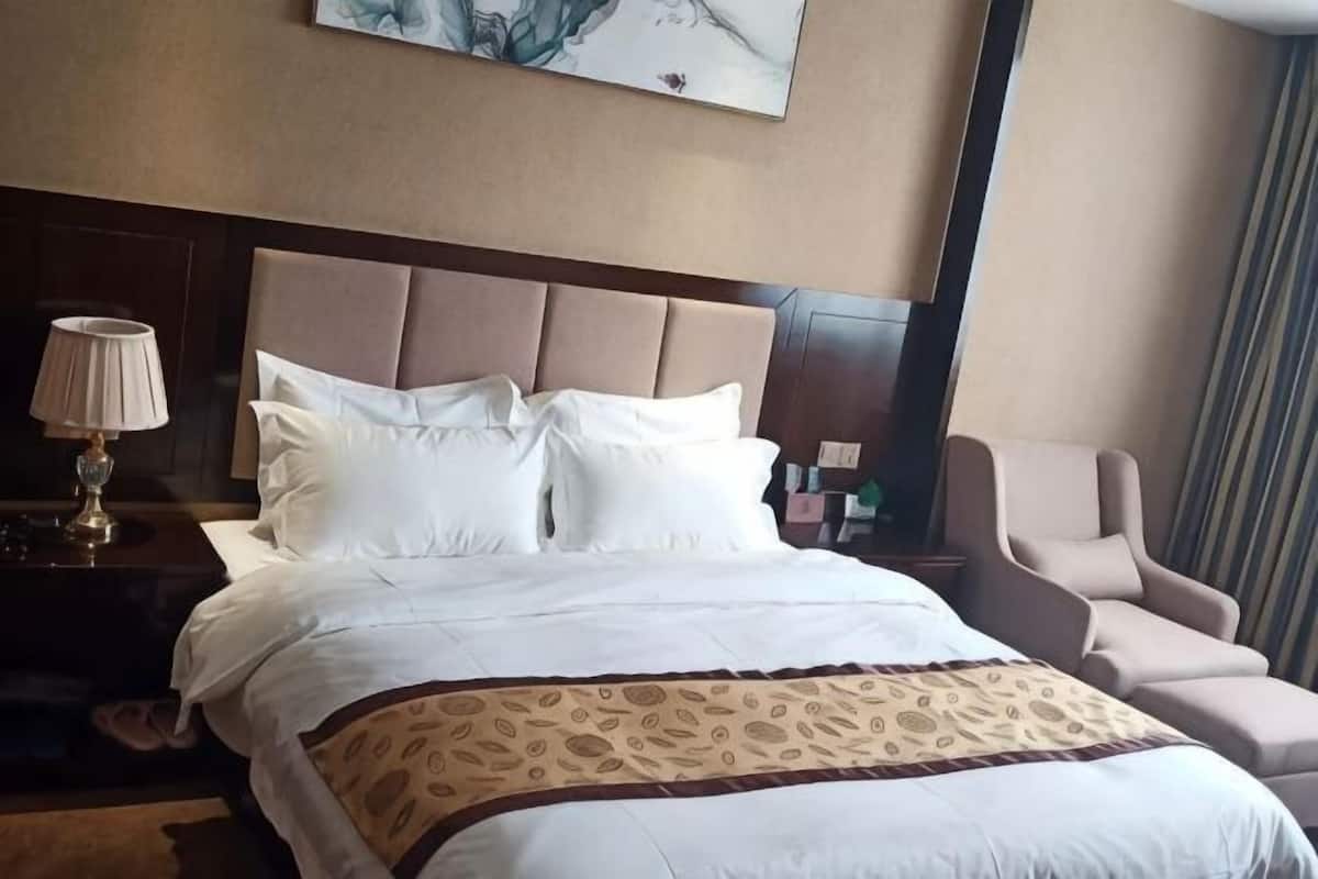 Une chambre d’hôtel avec un grand lit, une table de chevet avec une lampe, une chaise et un tableau au mur.