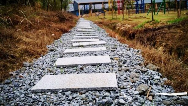 Ein Weg mit Steinplatten führt zu einem Gebäude, an dem ein Schild in einer Fremdsprache hängt.