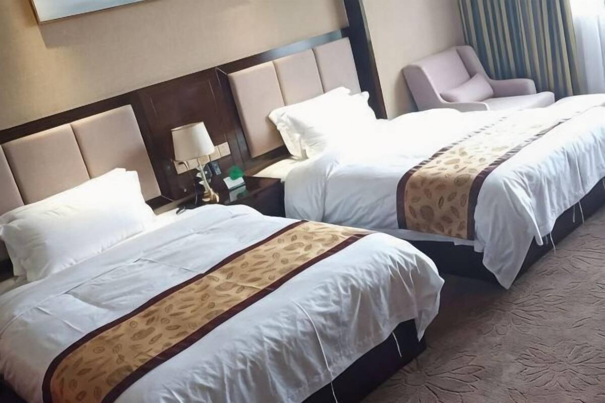 Une chambre d’hôtel avec deux lits, une table de chevet avec une lampe, une chaise et une vue sur un immeuble.