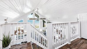 A white wooden interior with a high ceiling, a ceiling fan, and a view of the beach through large windows. - Beautiful Beachfront Home with Amazing Views, Steps to Beach (Bay City)