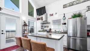 A modern kitchen with white cabinetry, a stainless steel refrigerator, and a bar area with two stools. - Beautiful Beachfront Home with Amazing Views, Steps to Beach (Bay City)