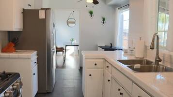 Une cuisine moderne avec des meubles blancs, un évier en acier inoxydable et un coin repas comprenant une table et des chaises.