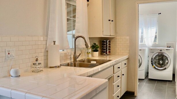 Una cocina moderna con un lavamanos, encimera y armarios empotrados. Se ve una lavadora al fondo.