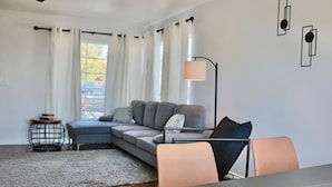 Una sala de estar moderna con un sofá gris, una mesa de centro redonda y una mesa de comedor con sillas.