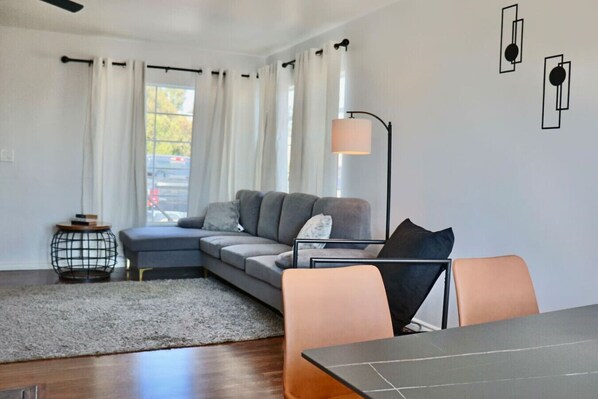 A modern living room with a grey sofa, a round coffee table, and a dining table with chairs. - Bakersfield Sunset Stay (Bakersfield)