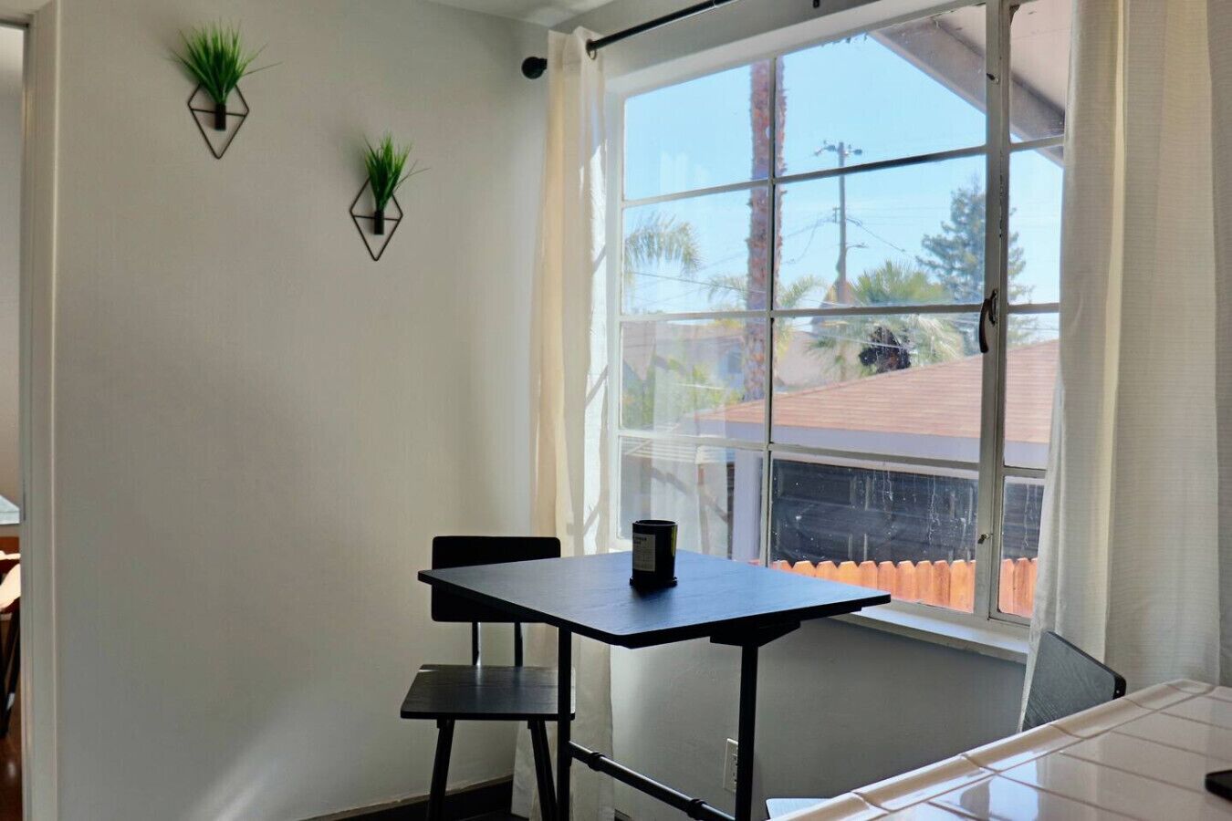 Une pièce dotée d’une grande fenêtre, d’une table avec deux chaises et de deux plantes fixées au mur.