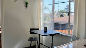 Una habitación con un ventanal grande, una mesa con dos sillas y dos plantas colgantes.