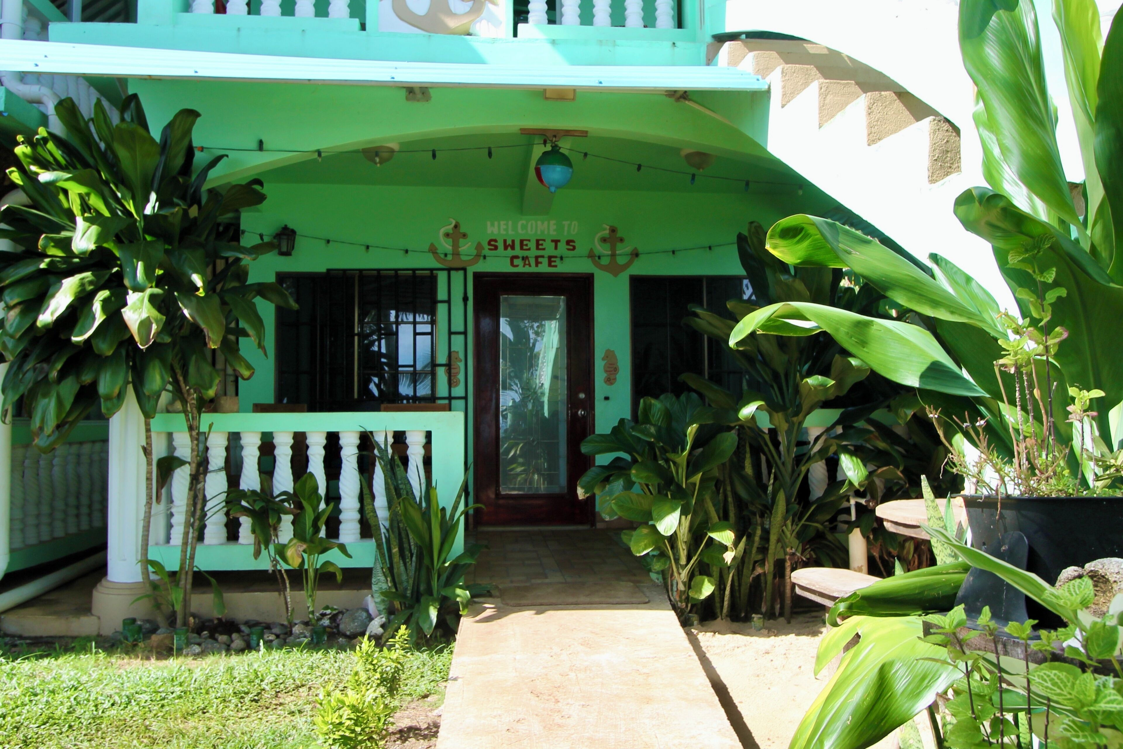 A green building with a sign reading "Welcome to Sweets Cafe" and a door.