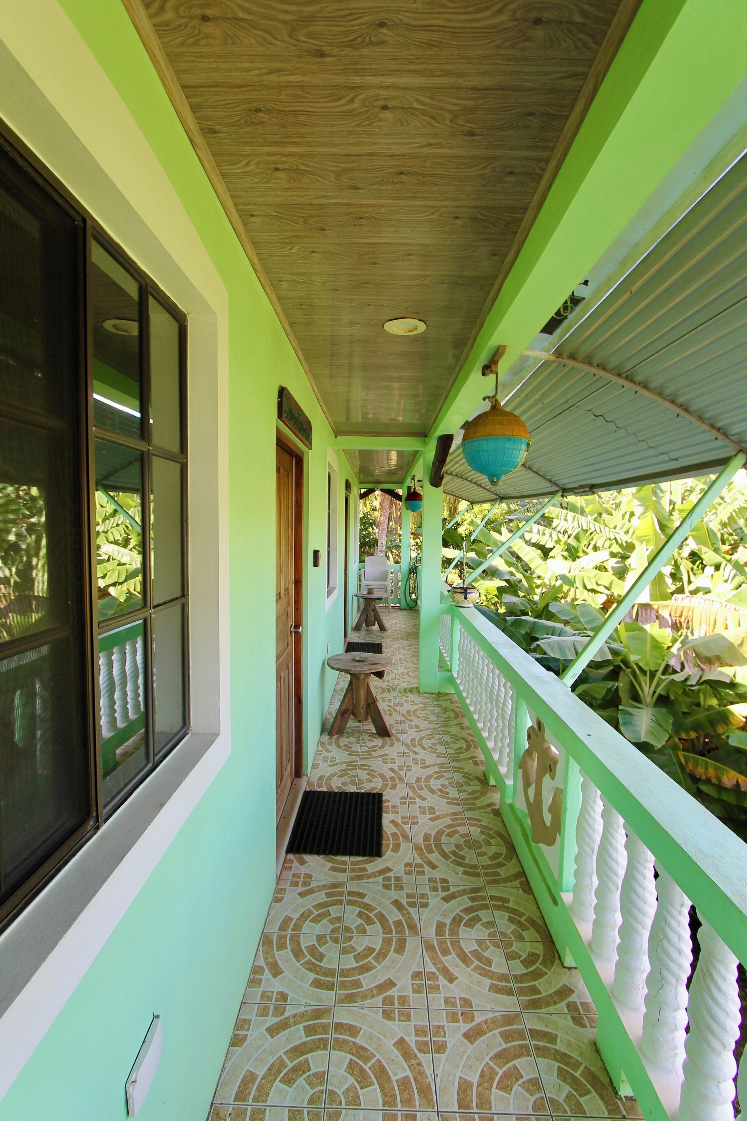 A covered corridor with a tiled floor, a wooden ceiling, and a green wall.