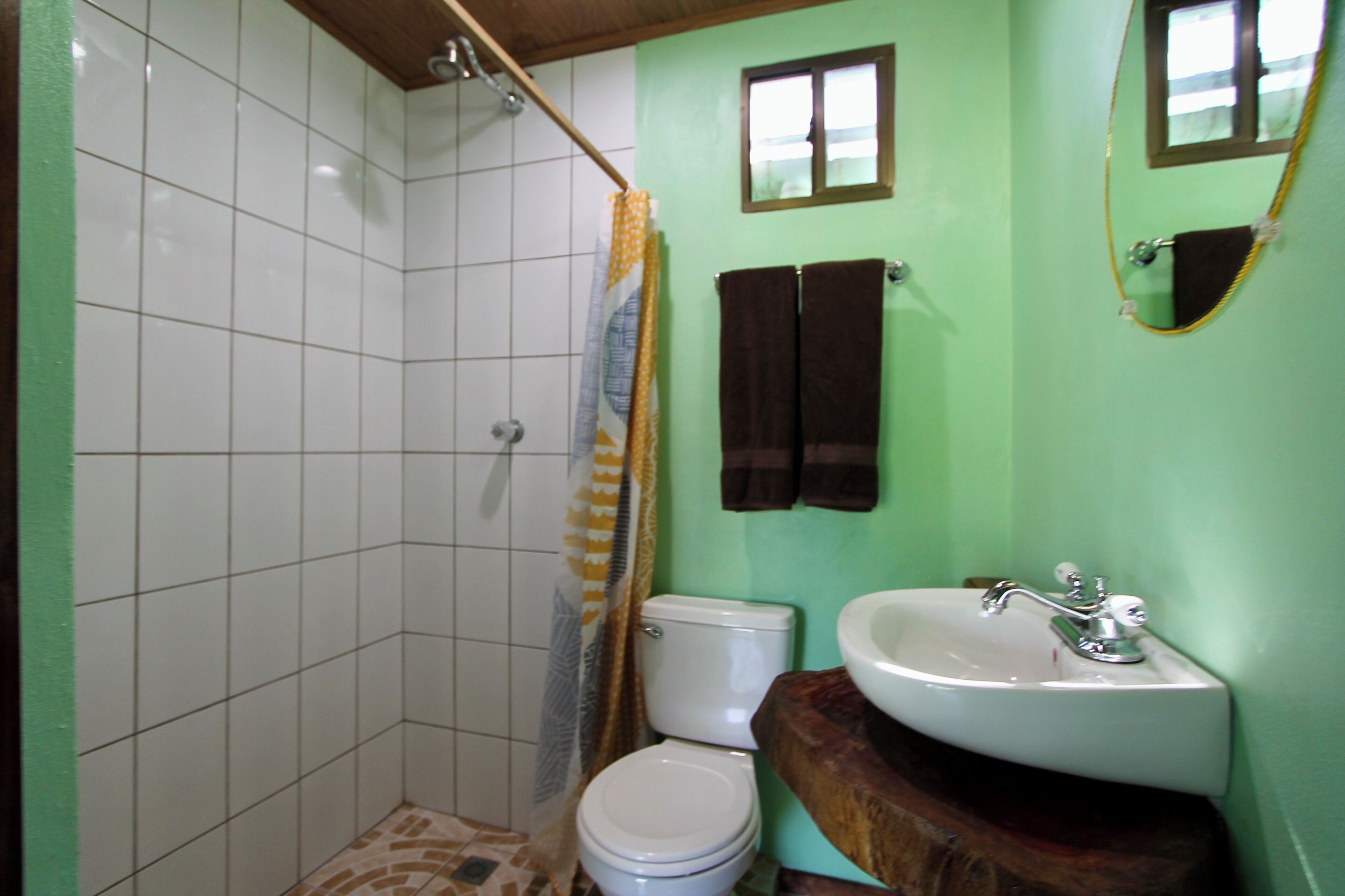 Et badeværelse med brusebad, toilet, vask og to håndklæder hængende på væggen.