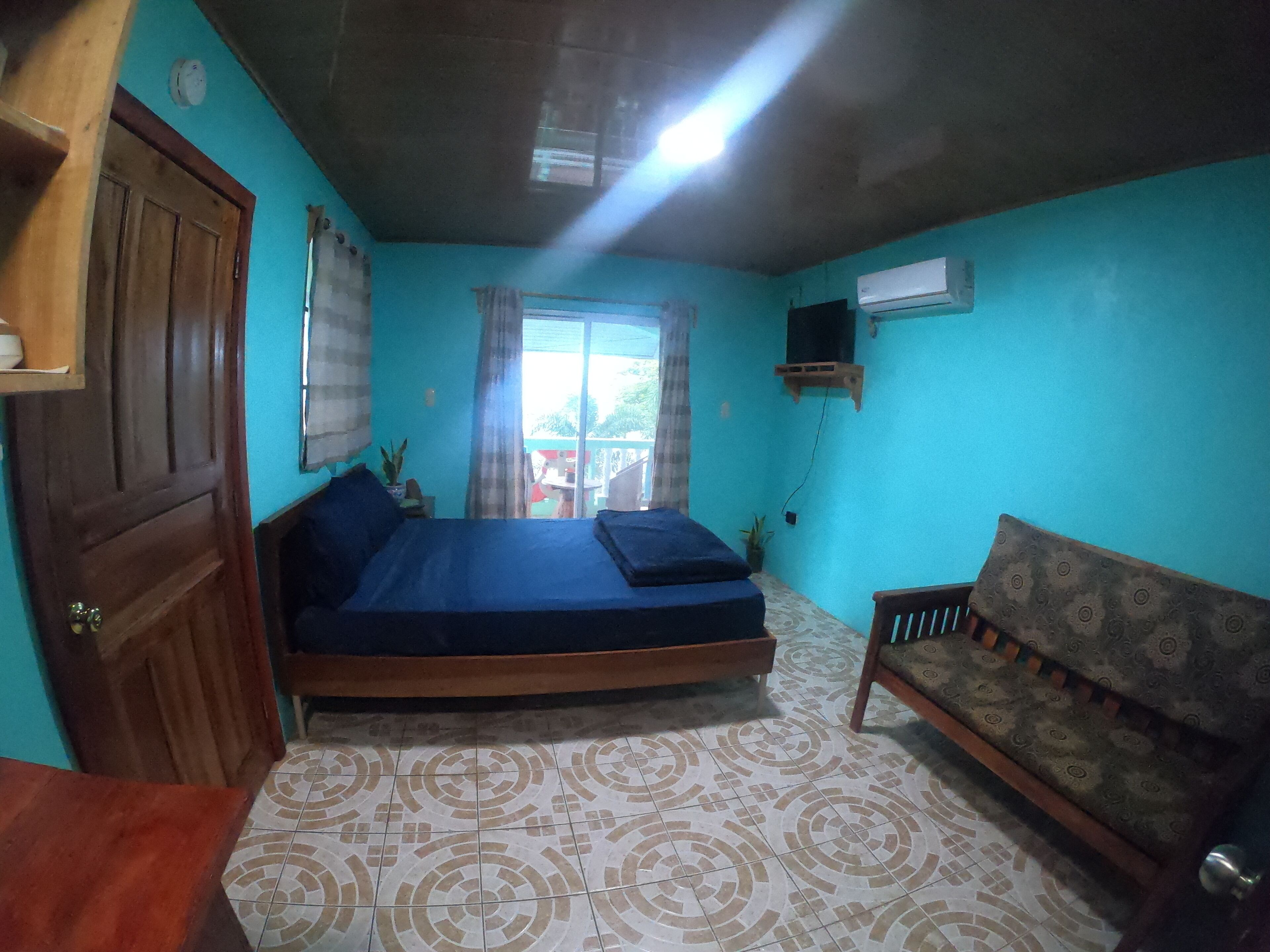 A room with a bed, a sofa, a wooden door, and a window with curtains.