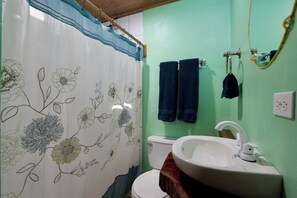 A bathroom with a floral shower curtain, a white sink, and two towels hanging on the wall.