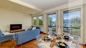 A modern living room with a blue sofa, a flat-screen TV displaying 'NETFLIX', and a dining area with a table set for a meal.